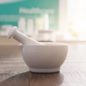 Mortar and pestle on the pharmacist's table and pharmaceutical products on the background